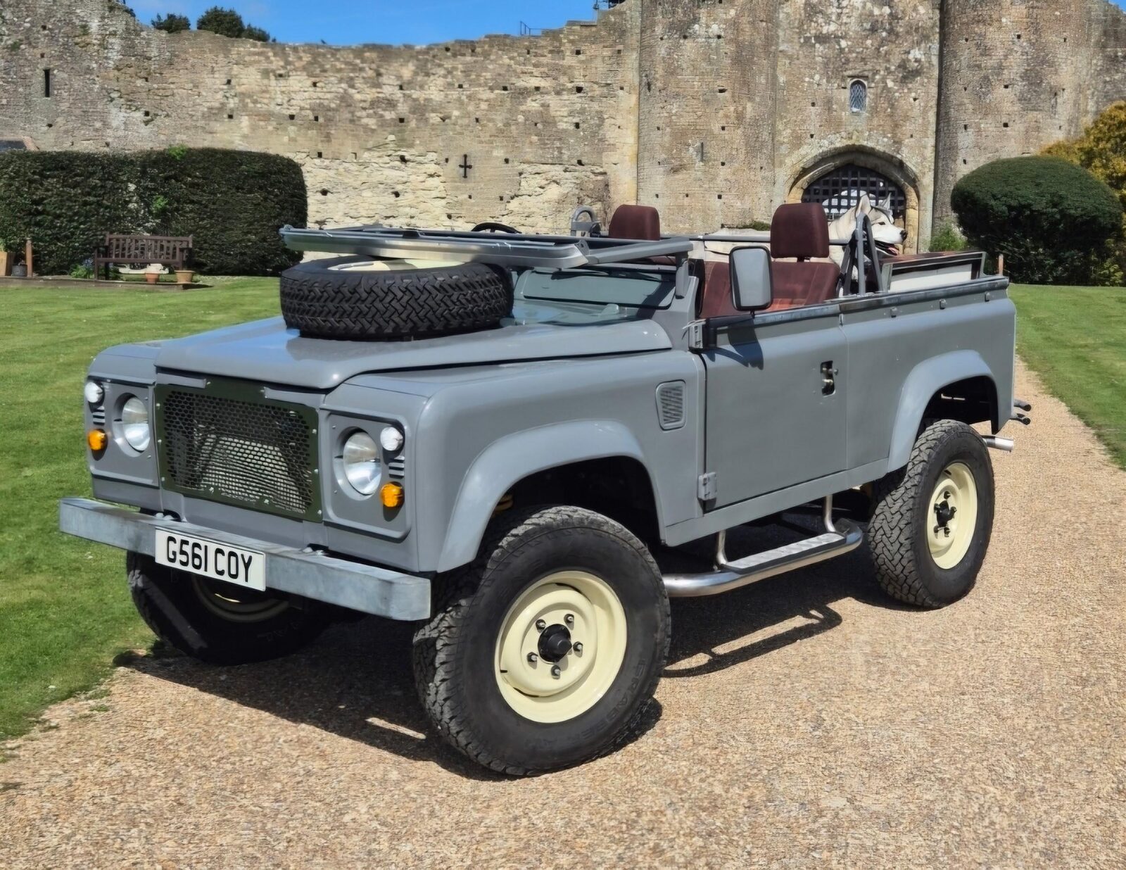 Rebuilt Land Rover Defender 90, Nardo grey, parked in front of a stone castle wall